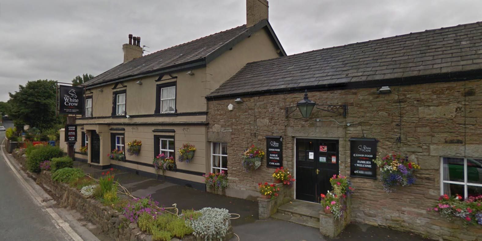 The front of the White Crow on Chorley Road, with hanging baskets and the black pub sign
